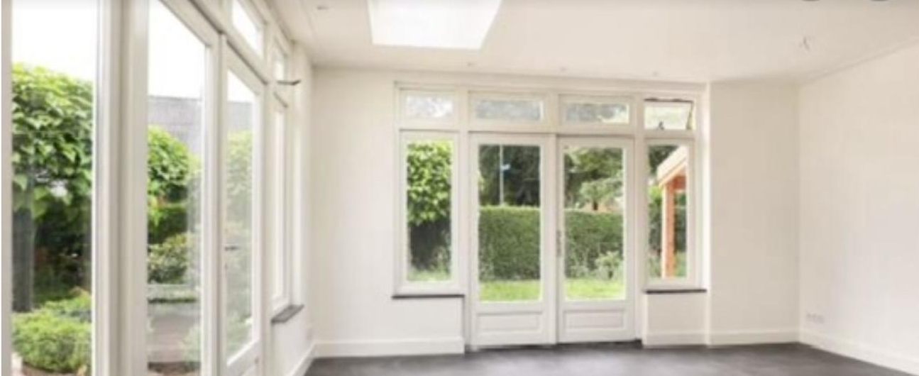 Lichte serre van binnen met witte houten kozijnen en tuindeuren