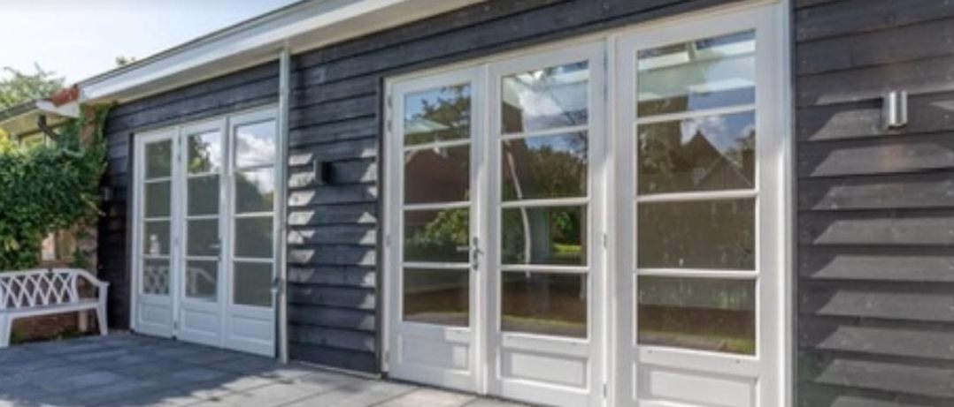 Witte openslaande tuindeuren in een gevel met donkere houten delen